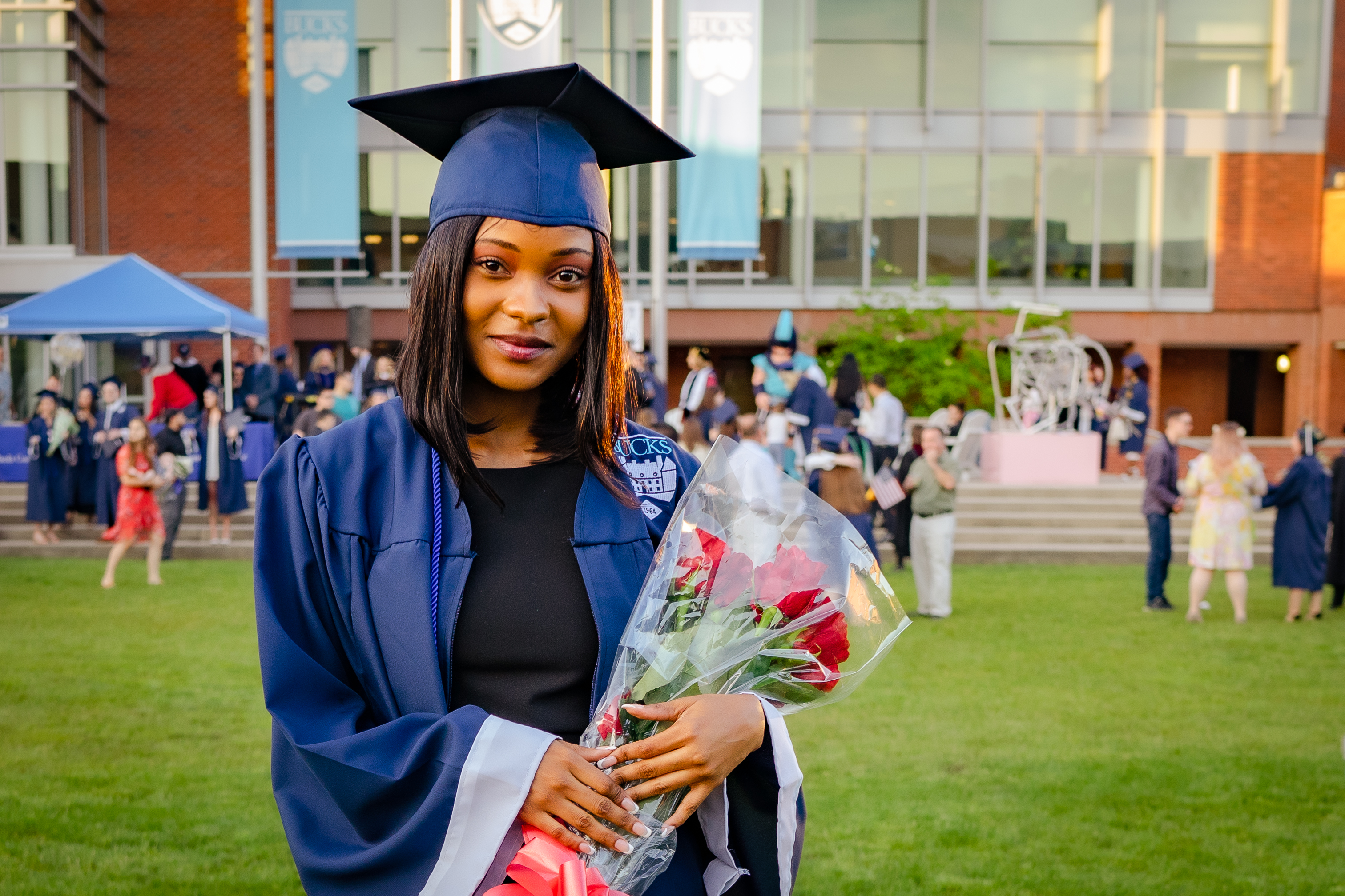 African American female in blue cap & gown holding flower bouquet